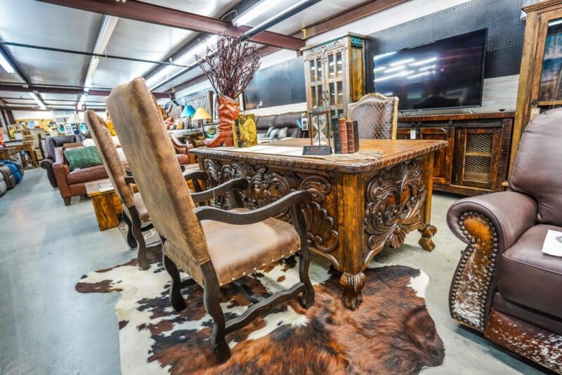 Carved wooden desk with leather chairs and rug.