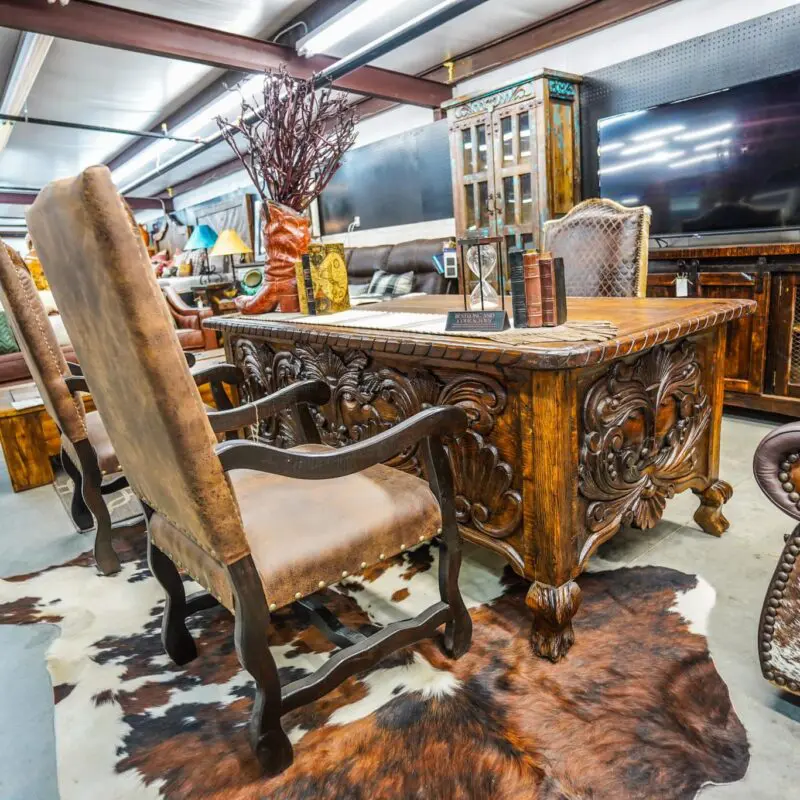 Carved wooden desk with leather chairs and rug.